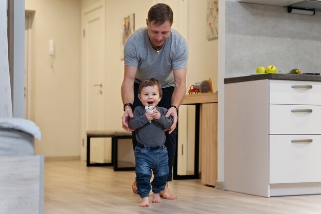 Padre de tiro completo ayudando a un niño a caminar en casa