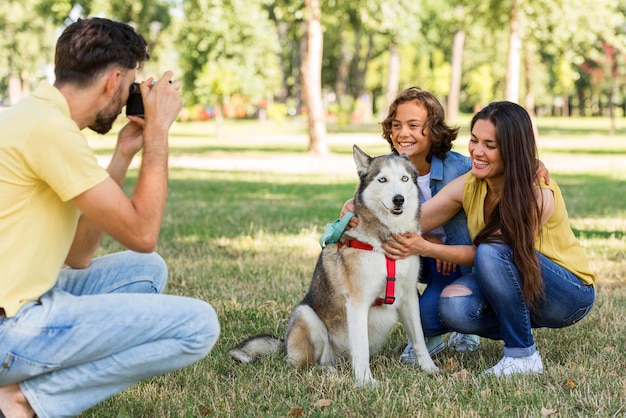 Padre tomando fotografías de madre e hijo con perro en el parque