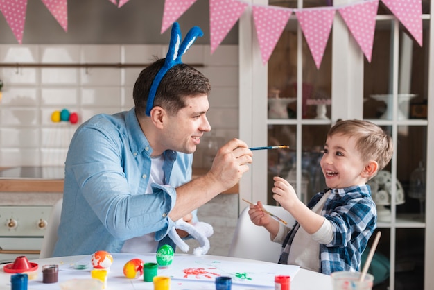 Foto gratuita padre tratando de pintar a su hijo para pascua