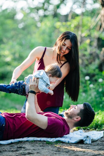 Padre tumbado en un parque con su bebé en alto y su madre ayudandole