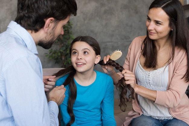 Padres de alto ángulo cepillando el cabello de su hija