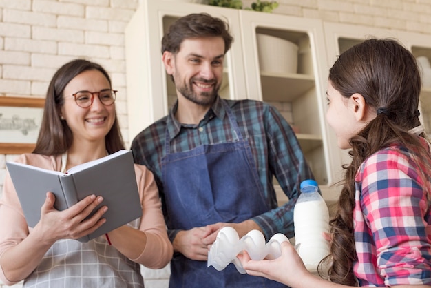 Padres de ángulo bajo enseñando a niña a cocinar