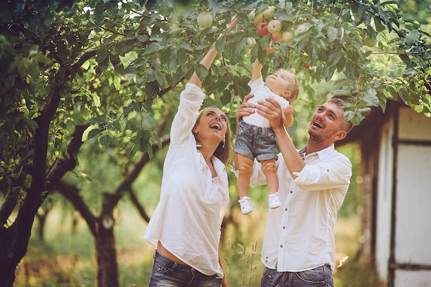 Los padres con el bebé disfrutando de un picnic en una granja con manzanos y cerezos.