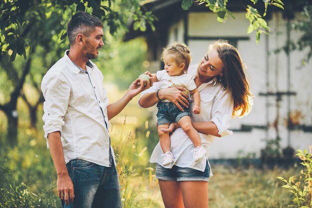 Los padres con el bebé disfrutando de un picnic en una granja con manzanos y cerezos.