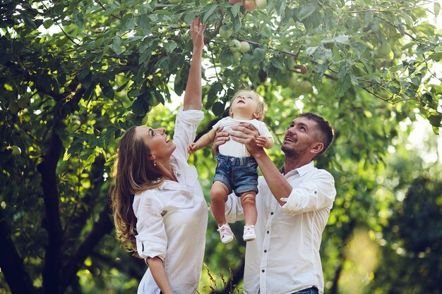 Los padres con el bebé disfrutando de un picnic en una granja con manzanos y cerezos.