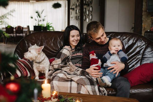 Padres con un bebé en navidad y un perro sentados en el sofá