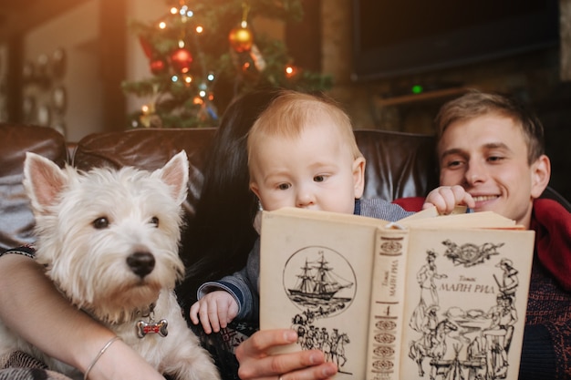 Padres con un bebé en navidad y un perro sentados en el sofá