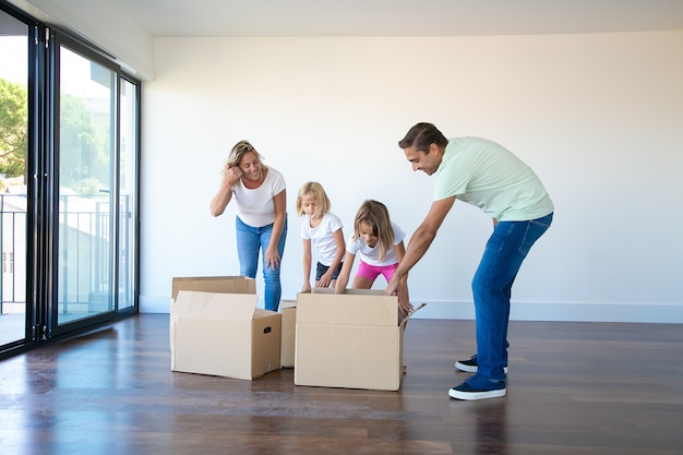 Los padres caucásicos desembalaje de cajas de cartón con hijas en una habitación vacía con balcón