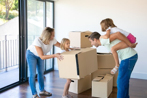 Padres e hijos felices celebrando la compra de un apartamento, abriendo cajas y divirtiéndose en su nuevo apartamento