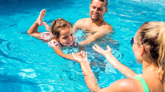 Padres enseñando a su hija a nadar en la piscina