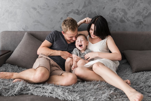 Los padres hacen cosquillas a su pequeño hijo mientras están sentados en el sofá