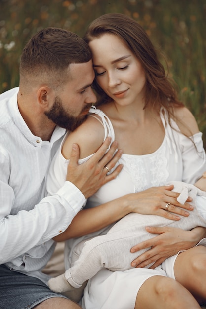 Padres con hija. Familia en un campo. Niña recién nacida. Mujer con un vestido blanco.