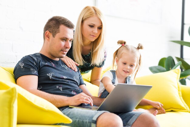 Padres con hija pequeña que usa la computadora portátil en la sala de estar en casa