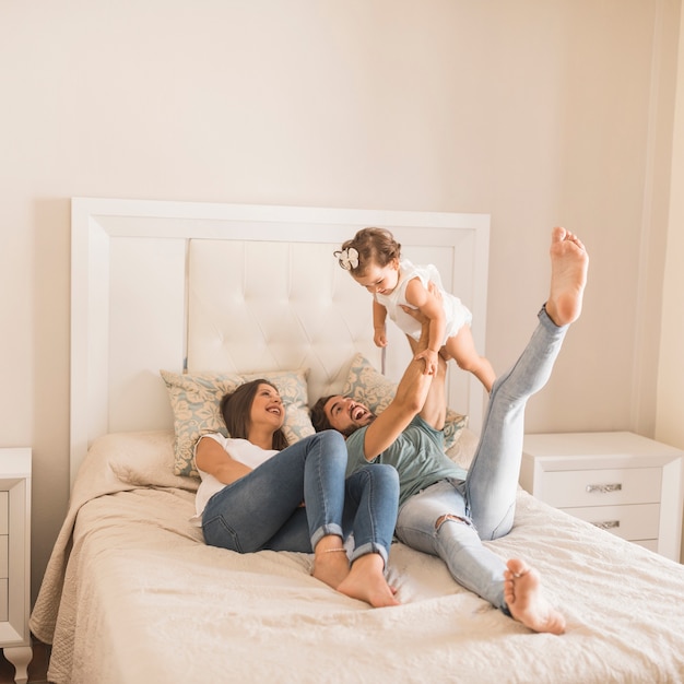 Padres jóvenes acostado en la cama y levantando a la hija