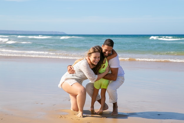 Foto gratuita padres jóvenes alegres abrazando a la pequeña hija