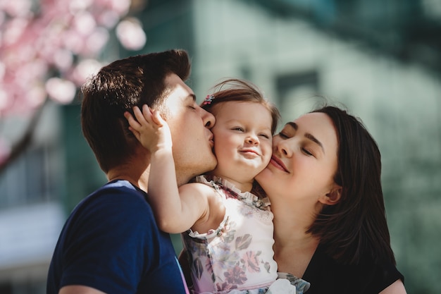 Los padres jóvenes felices con una pequeña hija se colocan debajo del árbol rosado floreciente afuera