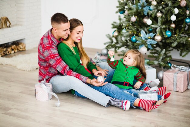 Padres jóvenes con hija al lado de árbol de navidad