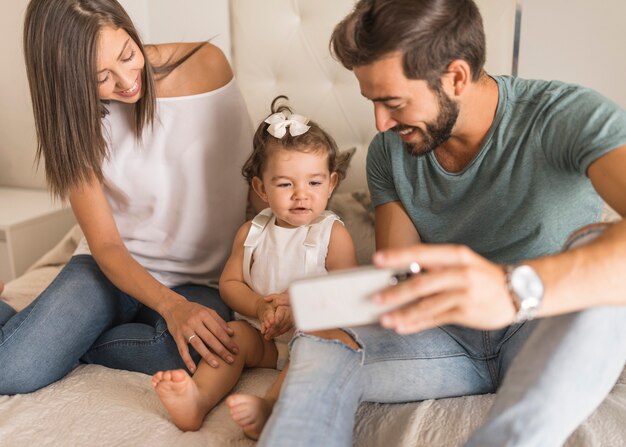 Padres jóvenes que muestran el teléfono inteligente a la niña