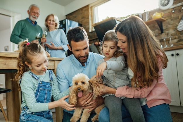 Los padres jóvenes y su pequeña hija disfrutan con un perro en casa. Los abuelos están parados en el fondo.