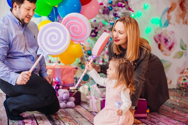 Los padres juegan con su pequeña hija en habitación rosa con árbol de Navidad