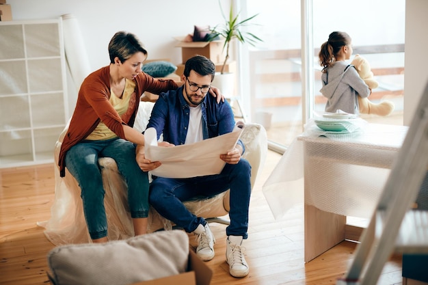 Padres de mediana edad analizando planos mientras se mudan a una nueva casa