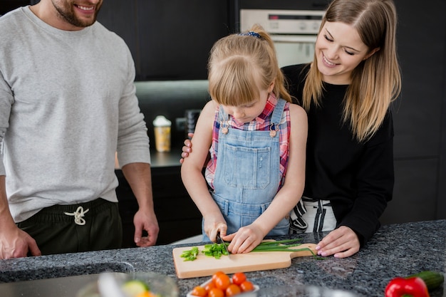 Padres mirando niña cortando verduras