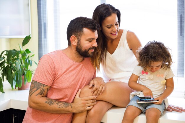 Padres mirando a su hija jugando en el teléfono inteligente