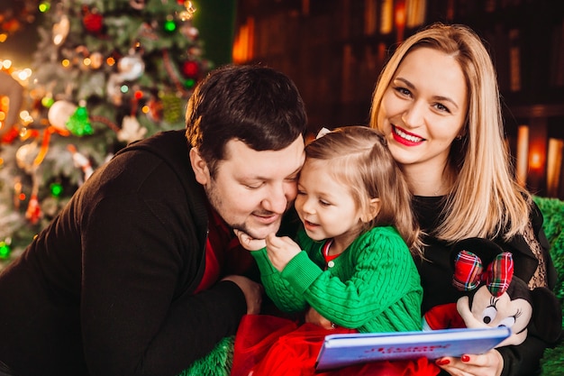 Los padres con niña rubia posan ante un árbol de Navidad en la habitación