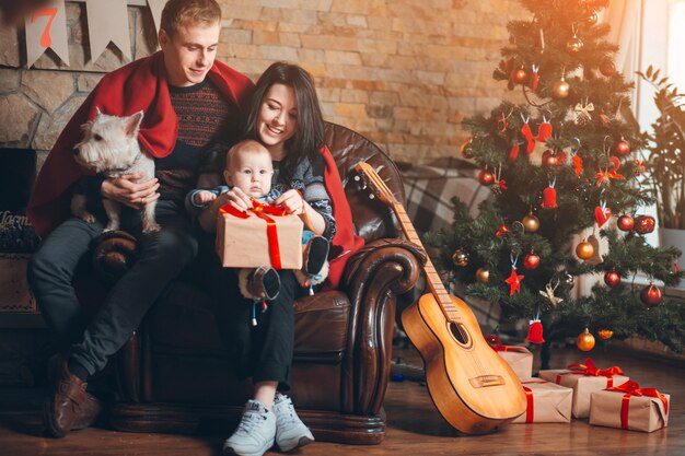 Padres con un perro y un bebé y una guitarra apoyada en el sofá