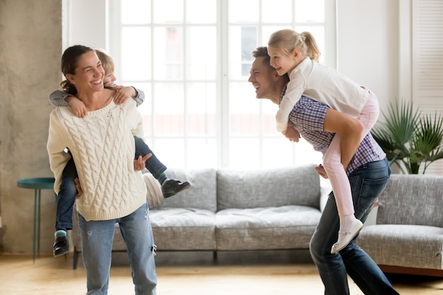 Foto gratuita padres que ríen dando a los niños a cuestas paseo jugando juntos en casa