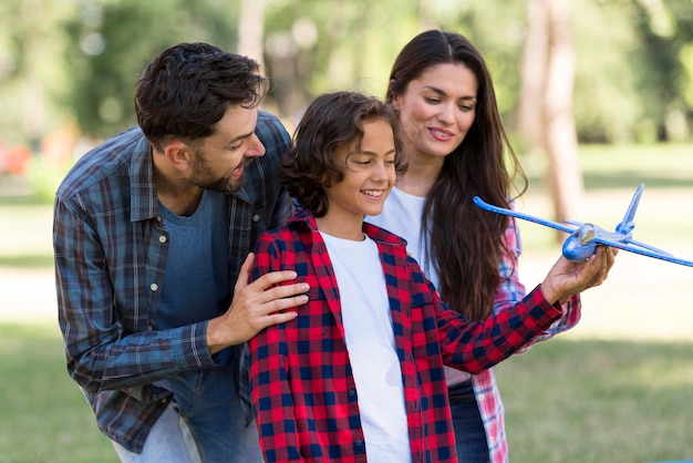 Padres sonrientes y niño jugando con avión juntos al aire libre