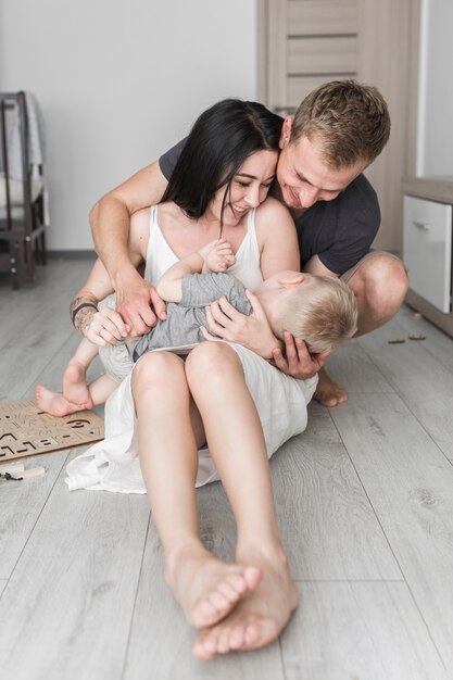 Padres sonrientes sentados en el piso de madera amando a su lindo hijo