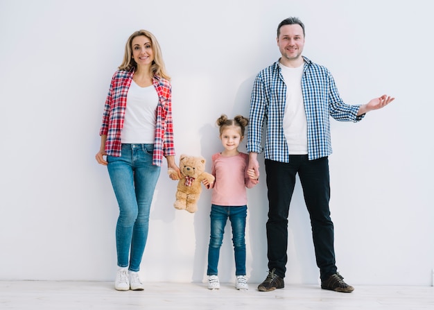 Padres sonrientes con su hija de pie contra la pared blanca