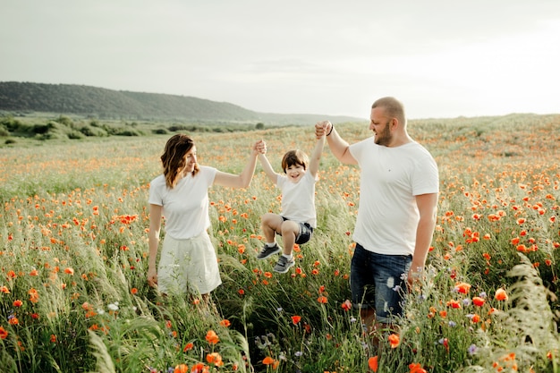 Foto gratuita los padres sostienen a su hijo por las manos entre el campo de amapolas