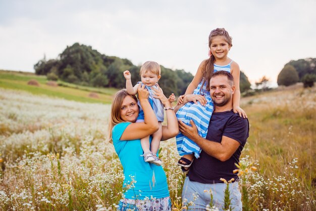 Los padres sostienen a sus hijos sobre los hombros, de pie en el campo