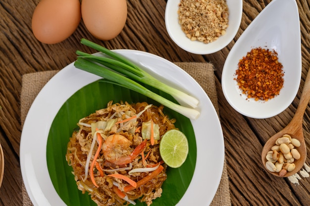 Padthai camarones en un plato blanco con limón y huevos en la mesa de madera.