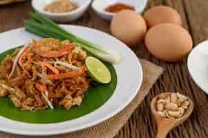 Foto gratuita padthai camarones en un plato blanco con limón y huevos en la mesa de madera.