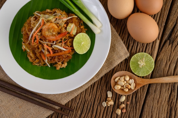 Foto gratuita padthai camarones en un plato blanco con limón y huevos en la mesa de madera.