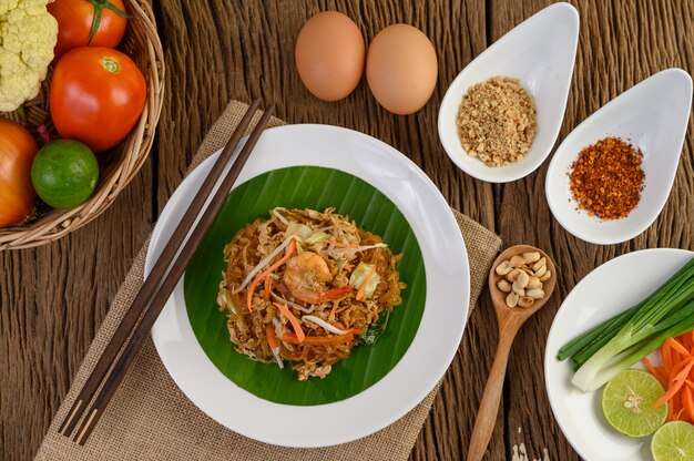 Padthai camarones en un recipiente negro con huevos, cebolla tierna y condimentos en la mesa de madera.