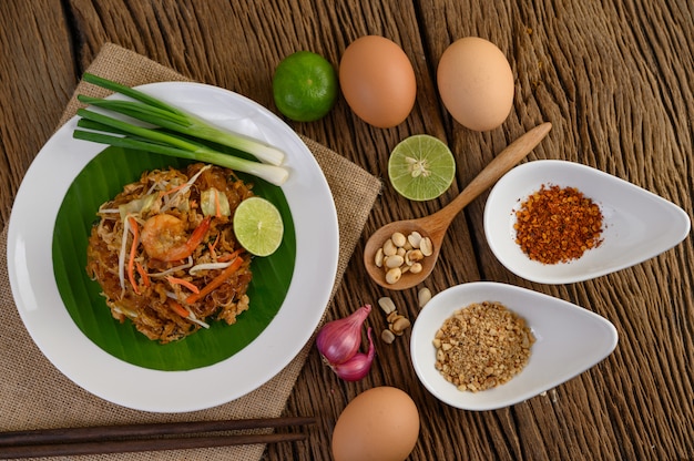 Padthai camarones en un recipiente negro con huevos, cebolla tierna y condimentos en la mesa de madera.