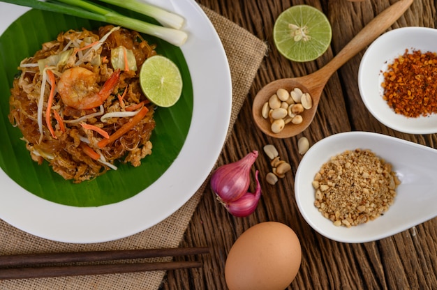 Padthai camarones en un recipiente negro con huevos, cebolla tierna y condimentos en la mesa de madera.