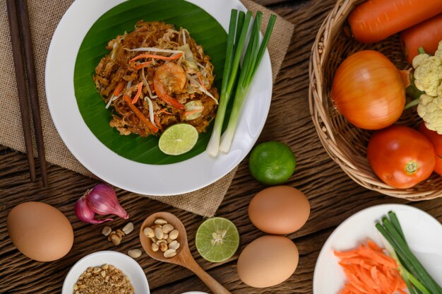 Padthai camarones en un recipiente negro con huevos, cebolla tierna y condimentos en la mesa de madera.