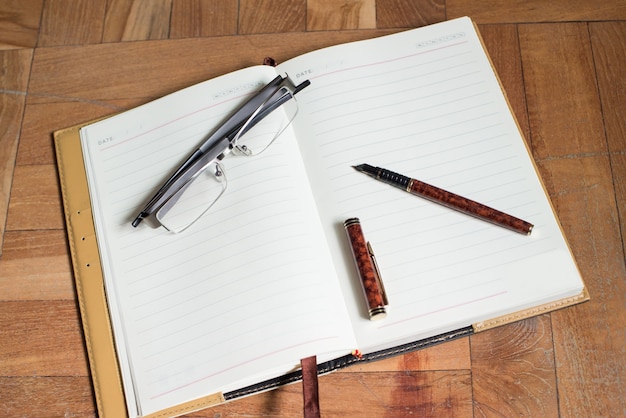 Páginas en blanco de una agenda con una pluma y un par de gafas