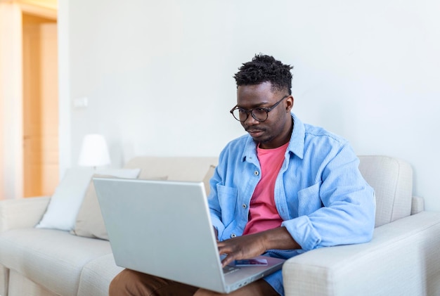 Pago por Internet Hombre alegre feliz mirando la pantalla de la computadora portátil mientras realiza un pago por Internet Hombre joven feliz con tarjeta de crédito y computadora portátil sentado en el sofá en casa Pago en línea