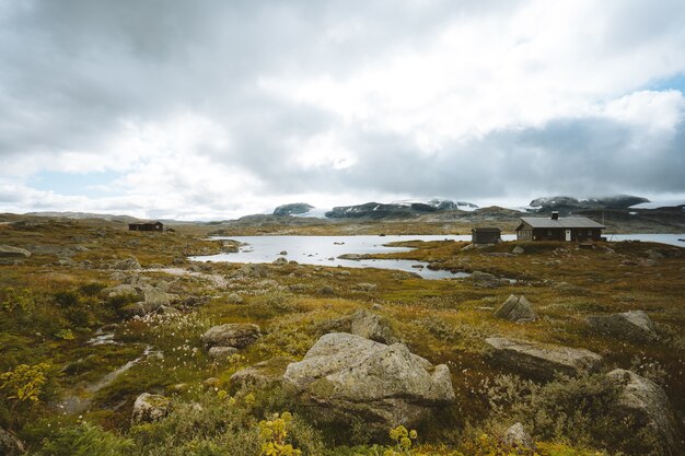 Paisaje de un campo rodeado de vegetación y cabañas bajo un cielo nublado en Finse, Noruega