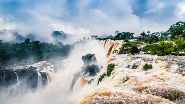 Paisaje de una cascada rodeada de bosques cubiertos de niebla bajo un cielo nublado