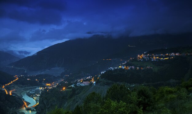 Paisaje de colinas cubiertas de edificios y bosques bajo un cielo nublado durante la noche