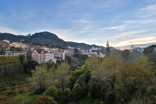 Paisaje de colinas cubiertas de edificios y bosques bajo un cielo nublado durante la puesta de sol