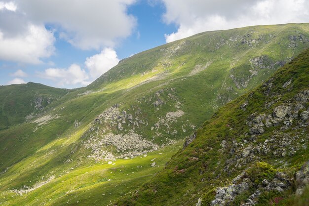 Paisaje de colinas cubiertas de rocas y vegetación bajo un cielo nublado y la luz del sol