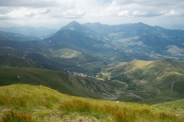 Paisaje de colinas cubiertas de vegetación con montañas rocosas bajo un cielo nublado en el fondo